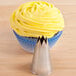 A cupcake with yellow frosting in a blue wrapper with an Ateco open star piping tip on top.