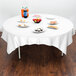 A table with food on it covered by a white Hoffmaster Cellutex table cover.