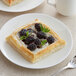 A square pastry with cream cheese and blackberries on top on a plate with berries and a fork.