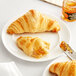 A white plate with two White Toque mini butter croissants and a jar of jam on a white background.