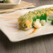 A rectangular melamine plate with a sushi roll topped with green vegetables.