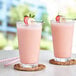 Two glasses of Capora strawberry banana smoothie with straws and fruit on them.