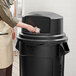 A woman using a Rubbermaid dome top to put a bag in a 55 gallon trash can.