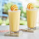 Two glasses of Capora orange smoothie with orange slices on top on a white surface.