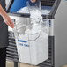 A woman pouring ice from a square container into an ice machine.