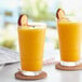 Two glasses of Capora peach smoothie with peach slices on the rim.