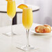 Two Acopa flute glasses of orange juice on a table with a croissant.