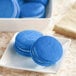 A white plate of blue macaroons with blue cookies on it.