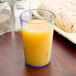 A Cambro slate blue plastic tumbler filled with orange juice on a table next to a sandwich.