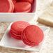 A plate of red macarons with a box of Chefmaster Natural Red Liqua-Gel Food Coloring on the side.
