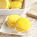 A plate of yellow macaroons with a yellow macaroon on a white surface.