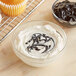 A bowl of white frosting with black swirls on a cupcake.