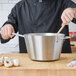 A person in a black coat stirring onions in a Vollrath stainless steel sauce pan.