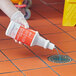 A hand wearing a glove pouring blue Noble Eco Enzo-Kleen liquid into a drain.