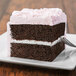 A slice of Rich's chocolate layer cake with pink frosting on a plate.