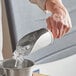 A person using a Choice stainless steel flour / breading scoop to pour ice into a metal bucket.