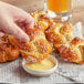 A hand dipping a Dutch Country Foods soft pretzel into mustard.