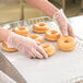 A person in plastic gloves holding a tray of Rich's fully finished glazed yeast donut rings.