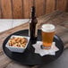 A bowl of pretzels and crackers and a glass of beer on a black Carlisle Griptite non-skid tray.