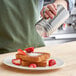A person using a Choice stainless steel shaker to sprinkle powdered sugar on a plate of french toast with strawberries.