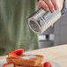 A hand using a Choice stainless steel shaker to sprinkle powdered sugar on French toast.