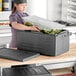 A woman in a chef's hat using a CaterGator black food pan carrier to store a plastic container full of vegetables.
