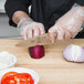 A person in gloves using a Mercer Culinary Genesis chef knife to slice a red onion on a cutting board.