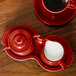 A red Fiesta creamer and sugar tray set on a table with a pitcher of milk and creamer.