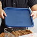 A person holding a blue lid over a Cambro blue plastic food storage container.