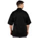 A man wearing an Uncommon Chef Venture Pro black short sleeve chef coat with mesh back.