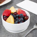 A white Arcoroc bowl filled with fruit on a table with a fork.
