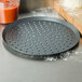 An American Metalcraft perforated hard coat anodized aluminum pizza pan on a counter with a pizza on it.