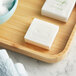 A wooden tray with Nourish cleansing grapefruit bar soap on it next to a white towel.