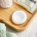 A wooden tray with round white Pharmacopia Verbena facial soap on a wood surface.