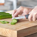 A hand using a Schraf Smooth Edge Paring Knife to cut a cucumber on a cutting board.