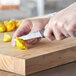 A person using a Schraf smooth edge paring knife to cut a yellow pepper on a wooden cutting board.