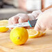A person in gloves using a Schraf serrated paring knife to cut a lemon.