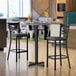 A Lancaster Table & Seating bar height table with a white and gray top and black base.