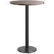 A round Lancaster Table & Seating bar table with a black metal base and a reversible wood table top.