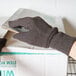 A hand in a brown Cordova jersey glove holding a box with a label.