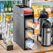 A KleanTake black countertop cup dispenser with straw dispenser slots and fast-changing gaskets filled with coffee cups.