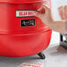 A person's hand putting a sticker on a red Avantco soup kettle.
