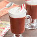 A glass mug of Ghirardelli peppermint hot chocolate with a candy cane in it.