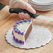 A person cutting an Enjay silver corrugated cake circle on a wooden surface.
