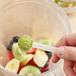 A hand holding a spoon of Add A Scoop Premium Matcha Green Tea Powder over a bowl of fruit.
