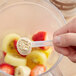 A hand holds a measuring spoon with Add A Scoop Fiber Blend supplement powder in a bowl of fruit.