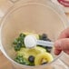 A hand holding a spoon with Add A Scoop Trim & Fit Supplement powder in a blender.