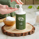 A hand holding a green and white Noble Eco Novo Terra hand lotion bottle.