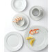 A group of Tuxton bright white china cups on a white surface with shrimp and lemon.