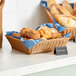 A dark brown woven plastic rattan basket filled with bread and muffins on a bakery counter.